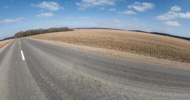 tiny planet transformation with curvature of space among fields on road in sunny day with sky and fluffy clouds video