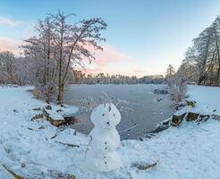 imagen terminado un congelado lago en el Mañana ligero con un monigote de nieve foto