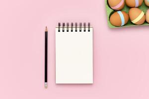 blanco cuaderno y lápiz en rosado antecedentes con huevo caja de cartón foto