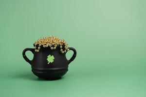 Black cauldron pot with a glitter clover and gold beads on green background photo