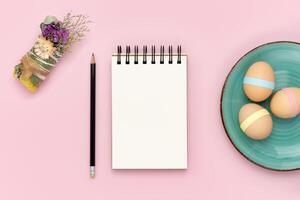 blanco cuaderno y lápiz en rosado antecedentes con mancha palo plato y Pascua de Resurrección huevos foto