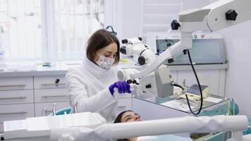 donna dentale chirurgo l'esame denti di paziente utilizzando operativo microscopio. moderno dentale attrezzatura nel odontoiatria. dentale strumenti per trattamento un' paziente con mal di denti nel il clinica video