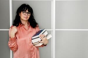 mayor mujer con lentes con un apilar de libros y lápiz en su manos foto