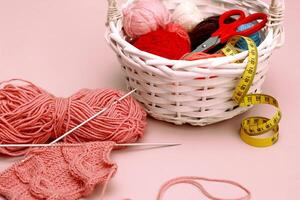 fragment of knitting with a pattern on knitting needles next to basket with multi-colored balls of thread photo