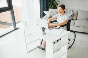 woman in a wheelchair works on the laptop PC in the home office with an assistance dog as a companion photo