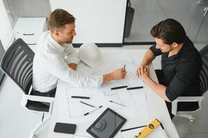 Two young architects with blueprints of a house standing in office, talking. photo