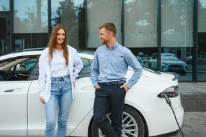 Young couple man and woman traveling together by new car having stop at charging station. photo