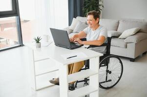 Middle age woman using laptop sitting on wheelchair at home photo