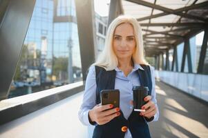 Beautiful Woman Going To Work With Coffee Walking Near Office Building. Portrait Of Successful Business Woman Holding Cup Of Hot Drink. photo