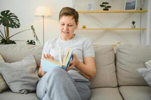woman in home sitting on sofa reading book. photo
