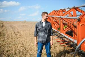 Handsome farmer with tablet standing in front of combine harvester during harvest in field. photo