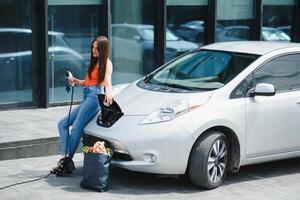 eco eléctrico coche concepto. mujer esperando eléctrico coche a cargar. foto