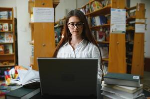 Universidad biblioteca hermosa inteligente caucásico niña usos computadora portátil, escribe notas para papel, ensayo, estudiar para clase asignación. enfocado estudiantes aprendiendo, estudiando para Universidad exámenes lado ver retrato foto