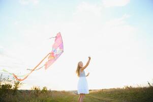 Little cute 7 years old girl running in the field with kite on summer day photo