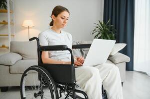 Female freelance programmer sitting in wheelchair and using computers while coding web game at home. photo