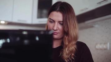 Close-up. Beautiful young business woman with long hair chatting on a mobile computer in black at home sitting at a table with a good mood. video