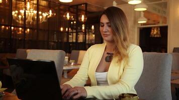 Beautiful business woman in business clothes with long beautiful hair prints on a mobile computer sitting at a table. Business style video