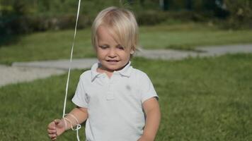 Attractive little boy in white clothes in a good mood walks on the grass in sunny weather video