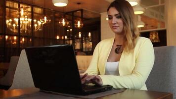 bellissimo attività commerciale donna nel attività commerciale Abiti Lavorando utilizzando un' mobile computer seduta a un' tavolo nel un' bar avendo un' bene umore. video