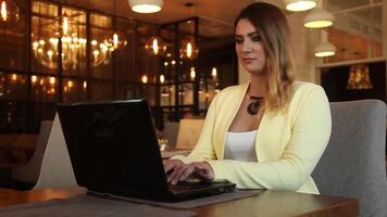 lindo o negócio mulher dentro o negócio roupas trabalhando usando uma Móvel computador enquanto sentado às uma mesa dentro uma cafeteria tendo uma Boa humor.hd. video