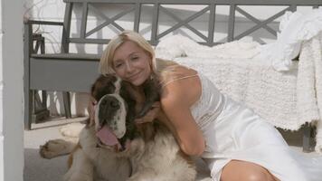 jung blond Mädchen Umarmungen ein groß Hund Sitzung auf ein Weiß Veranda beim Zuhause video
