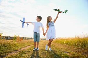 corriendo chico y niña participación dos verde y azul aviones juguete en el campo durante verano soleado día foto