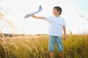 el niño carreras con un juguete avión. hijo Sueños de volador. contento niño, chico, carreras en el Dom jugando con un juguete avión en el verano campo foto