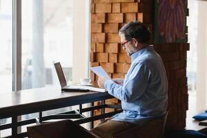 Business, technology and people concept , senior businessman with laptop computer drinking coffee at modern cafe. photo