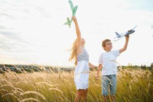 corriendo chico y niña participación dos verde y azul aviones juguete en el campo durante verano soleado día foto