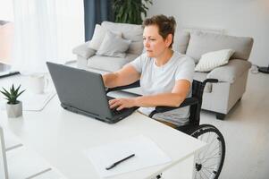 Freelancer in wheelchair using laptop near notebook and papers on table photo