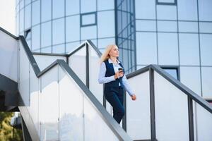 Beautiful Woman Going To Work With Coffee Walking Near Office Building. Portrait Of Successful Business Woman Holding Cup Of Hot Drink. photo