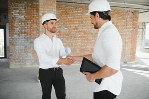 A front view of two smart architects with white helmets reviewing blueprints at a construction site on a bright sunny day photo