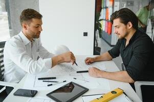 Two engineering working together and using digital tablet looking blueprint and analysis with architectural plan on desk photo