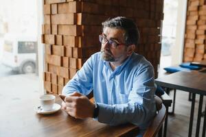 tomando tiempo para el descanso para tomar café. hombre maduro confiado en ropa formal tomando café y escribiendo un mensaje en el teléfono móvil mientras está sentado en el restaurante foto