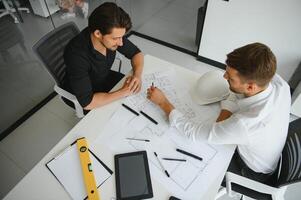 Two engineering working together and using digital tablet looking blueprint and analysis with architectural plan on desk photo