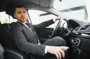 hombre de estilo y estatus. un joven apuesto con traje completo sonriendo mientras conduce un auto foto