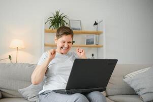 Elderly female sit on couch holding on lap laptop search information, check or typing e-mail, spend time on-line, modern tech, easy interesting pastimes services for retired older generation concept. photo