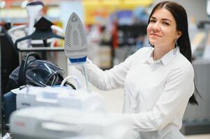 Beautiful young woman buying steam iron in store. photo