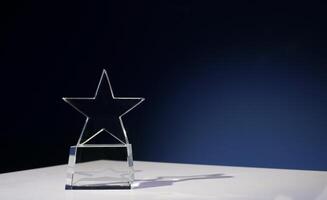 Star-shaped award made of glass on a white table with a spotlight on it and copy space photo