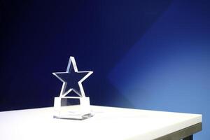 Star-shaped award made of glass on a white table with a spotlight on it and copy space photo