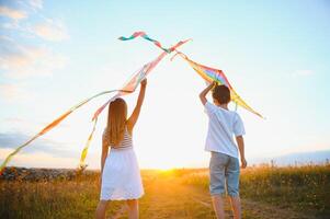 hermano y hermana jugando con cometa y avión a el campo en el puesta de sol. foto