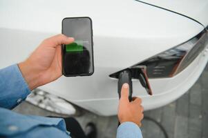 Charging Electric car Looking at App On Mobile Phone. Close up of smartphone screen. Hand holding smart device. Mobile application for eco transportation photo