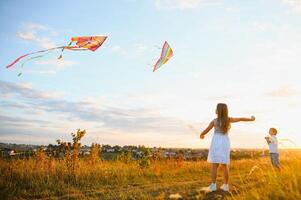 hermano y hermana jugando con cometa y avión a el campo en el puesta de sol. foto