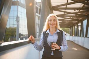 Beautiful Woman Going To Work With Coffee Walking Near Office Building. Portrait Of Successful Business Woman Holding Cup Of Hot Drink. photo