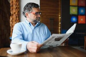 activo mayor hombre leyendo periódico y Bebiendo café en restaurante foto