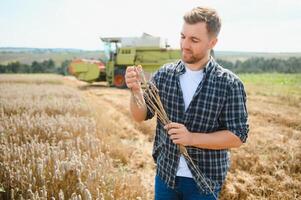 Handsome farmer with tablet standing in front of combine harvester during harvest in field. photo