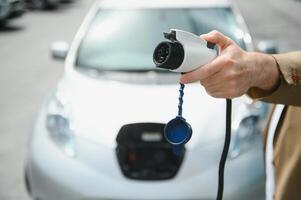 handsome man holding charging cable at electric charging station point standing near his new car. photo