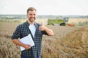 Handsome farmer with tablet standing in front of combine harvester during harvest in field. photo
