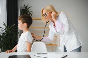 Female doctor examining boy by stethoscope photo