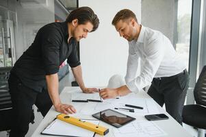 Two engineering working together and using digital tablet looking blueprint and analysis with architectural plan on desk photo